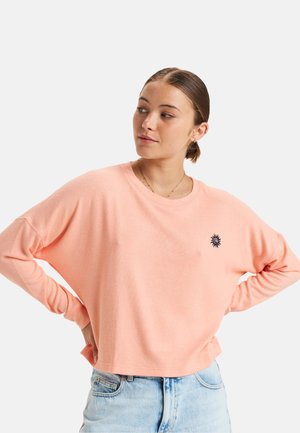Light pink long-sleeve sweatshirt with a relaxed fit, featuring a small black sun emblem on the chest and soft, textured fabric.