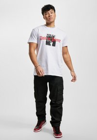 Hvit bomulls-T-skjorte med rødt tekst "Pain to Power," kombinert med svarte cargobukser og svarte/røde joggesko, med en avslappet passform og lommer.