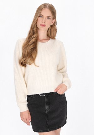 Cremefarvet ribstrikket sweater med lange ærmer og rund halsudskæring, parret med en sort denimnederdel. Sweateren har en afslappet pasform og en blød tekstur.
