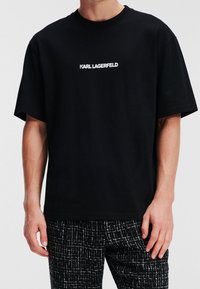 Svart bomulls t-shirt med korta ärmar, med en vit "KARL LAGERFELD" logotyp tryckt över bröstet. Enkel, avslappnad passform.