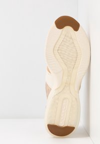 Sula på en beige sneaker med genomskinlig gummisula och bruna greppdynor, som visar strukturerade mönster och "COACH"-märkning på sulan.