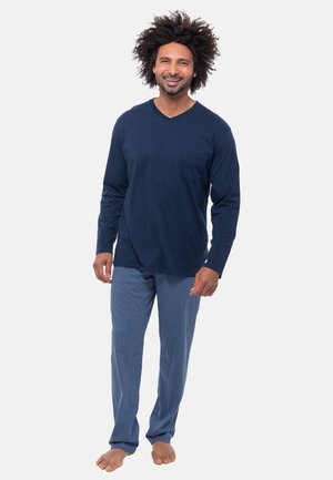 Marineblauw langemouwen V-hals shirt met een zak, gecombineerd met blauw-witte geruite pyjamabroek, blote voeten.