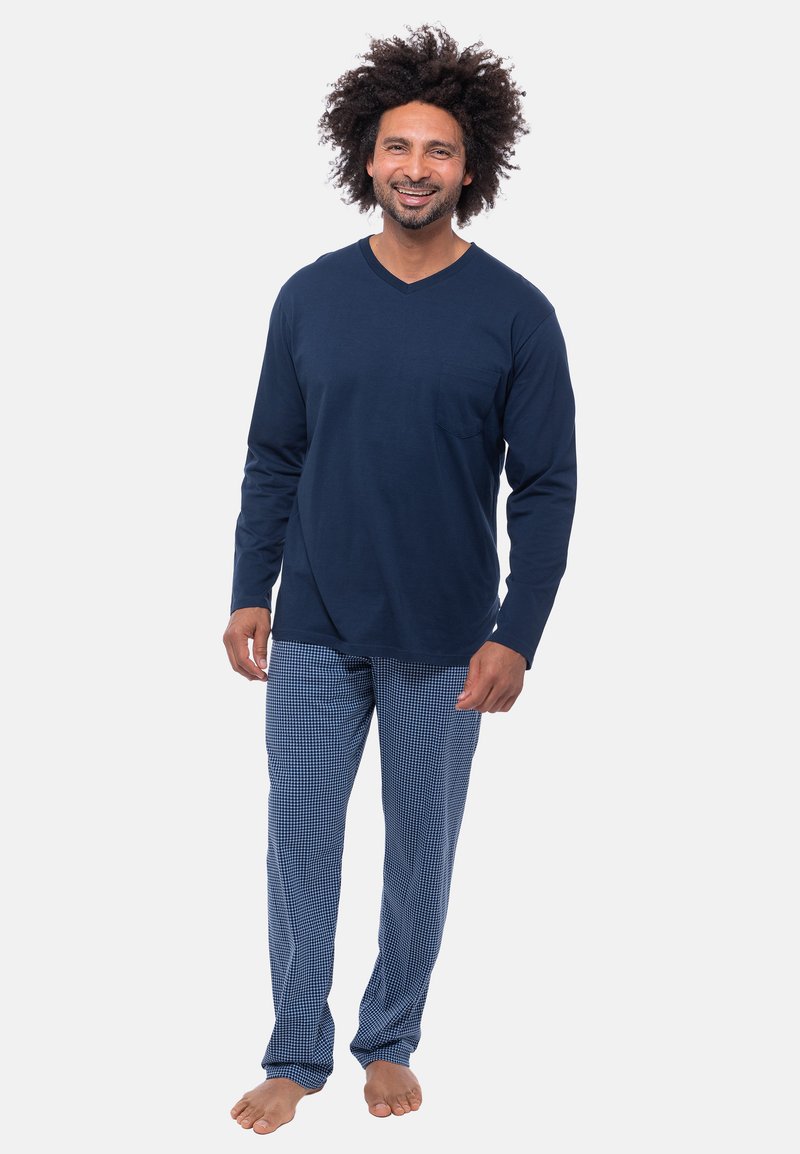 Laivansininen pitkähihaisen V-neck-paita, jossa on tasku, yhdistettynä sinivalkoraidallisiin yöpuvun housuihin, jalassa paljaat varpaat.