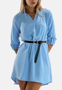 Vestito camicia azzurro chiaro con scollo a V, maniche lunghe arrotolate e cintura nera con fibbia circolare dorata. Tessuto morbido e lavorato.