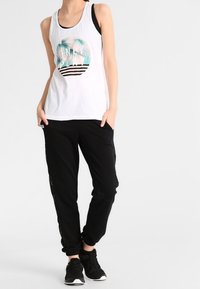 Biały top na ramiączkach z tropikalnym wzorem i czarnymi paskami, w połączeniu z czarnymi spodenkami dresowymi z bocznymi detalami. Czarne sneakersy.