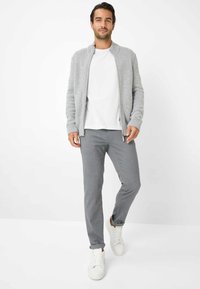Grauer Strickcardigan mit hohem Kragen, kombiniert mit einem weißen T-Shirt und hellgrauen Hosen. Weiße Sneaker runden das Outfit ab.