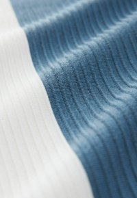 Tejido acanalado con franjas alternas de azul claro y blanco. El material parece suave y texturizado, mostrando líneas finas y un patrón distintivo.