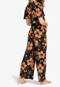 Mono floral negro con mangas cortas, que presenta grandes flores naranjas y hojas verdes. Ajuste suelto con una cintura ceñida y piernas anchas.