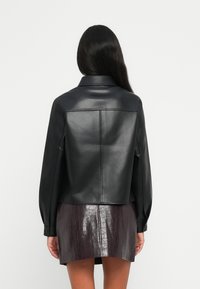 Svart skinnjakke med en cropped design, løse ermer og krage. Kombinert med et teksturert, mørk lilla miniskjørt.