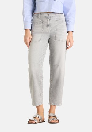 Vrouw die lichtgrijze high-waist recht gesneden jeans met grote voorzakken draagt, een cropped lichtblauw shirt en metallic zilveren sandalen.