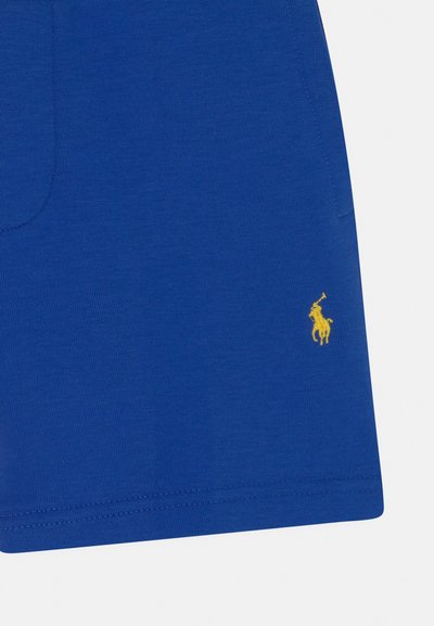 Shorts de algodão azuis com uma textura suave, apresentando um logótipo de jogador de polo bordado amarelo no lado inferior esquerdo.