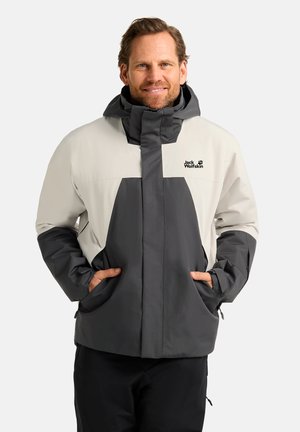 Veste imperméable grise et crème avec fermeture éclair sur le devant, grandes poches et capuche. Présente un logo sur le côté supérieur gauche. Coupe régulière et tissu durable.