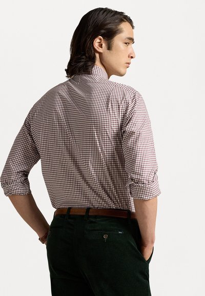 Kockás ing piros és fehér színben, slim fit szabású, gombos gallérral, feltekert ujjal, zöld kordbársony nadrággal és barna övvel párosítva.