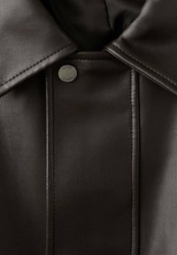 Chaqueta de cuero marrón con cuello estructurado, que presenta un botón a presión plateado y detalle de costuras visibles a lo largo de las costuras.