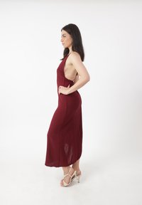 Robe maxi sans manches bordeaux avec découpes latérales, tissu fluide et légère texture. Associée à des sandales à talons beiges.