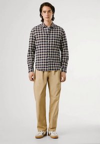 Camicia con bottoni a quadri in blu navy e crema, abbinata a pantaloni beige e sneaker bianche. Messa in evidenza del motivo a griglia e della vestibilità casual.