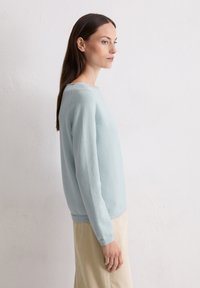 Helles blauer Rundhalspullover mit langen Ärmeln, weicher Textur und gerippten Bündchen, getragen mit einem pastellfarbenen Rock. Schlichtes Design.