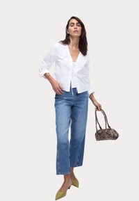 Camicia bianca a bottone, jeans a gamba larga azzurri, mule verdi e borsa in pelle di serpente marrone. Design semplice, texture liscia.