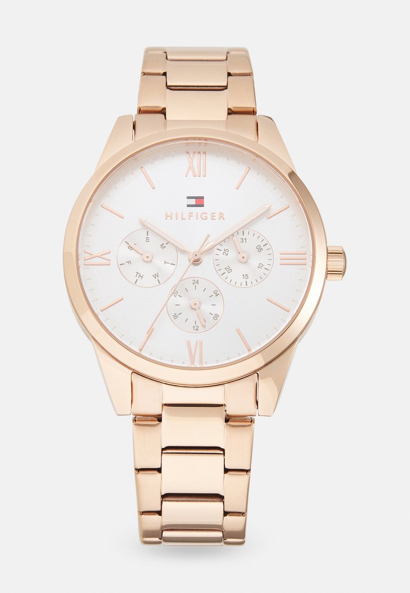 Reloj de metal color oro rosa con esfera blanca, marcadores de números romanos, tres subesferas y una pulsera pulida. Presenta detalle del logotipo.