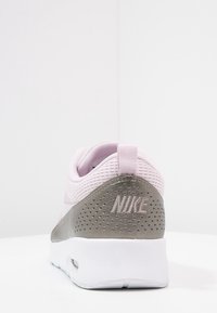 Zapatilla Nike en rosa claro con un upper texturizado, contra de talón gris, acentos perforados y suela blanca. Logotipo mostrado en el talón.