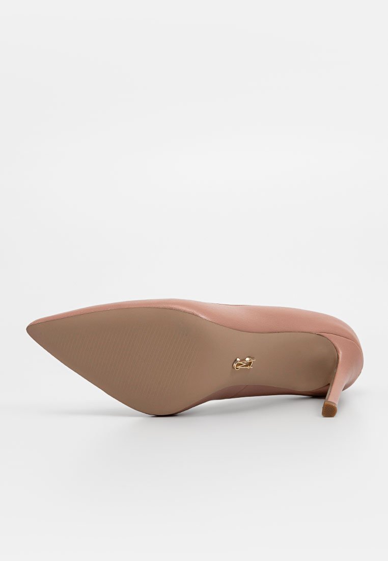 Chaussure à talon haut nude à bout pointu vue de la semelle avec un petit logo doré près de l'arche et un talon élancé.