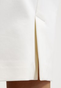 Valkoinen hame, jossa on sivuaukko, sileä pinta ja jämäkkä muotoilu, joka näyttää siistin reunan helmoissa ja sisävuorissa.