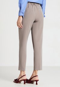 Pantalons gris clair à taille élastique avec une coupe fuselée et une texture lisse. Portés avec des escarpins slingback rouges brillants ornés de nœuds.