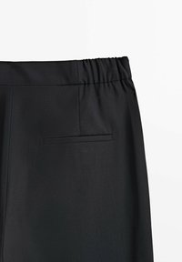 Zwarte broek met een elastische tailleband, een gladde textuur en een enkele achterzak met een platte sluiting, gericht op functionaliteit.