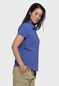 Short-sleeved button-up shirt in bright blue fabric, featuring a spread collar, two side pockets, and a streamlined silhouette.