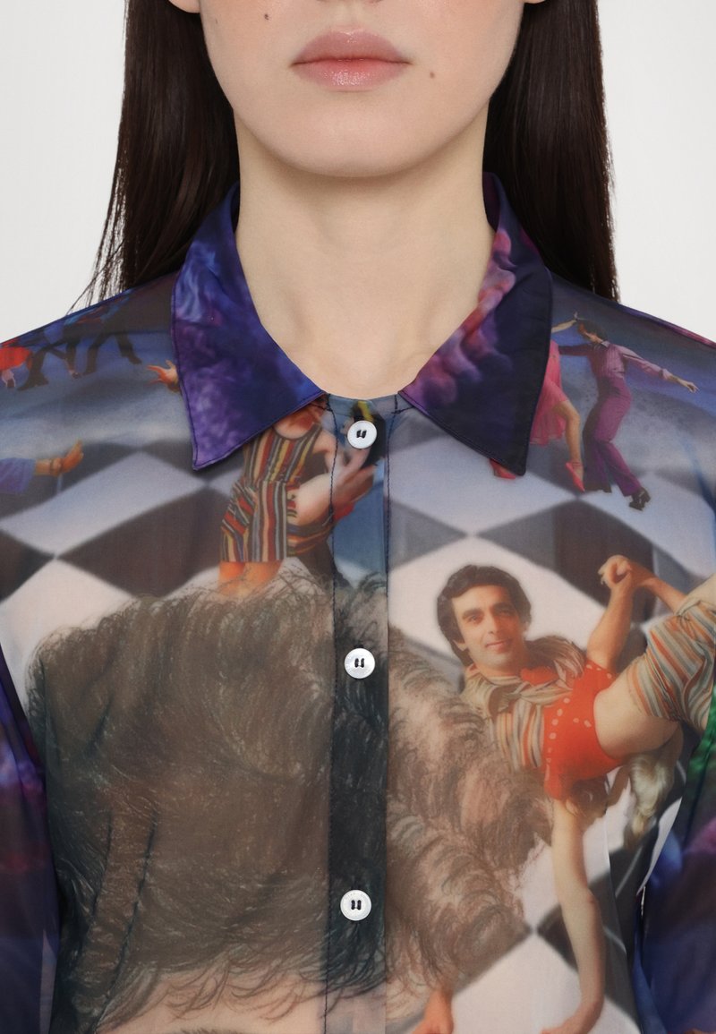 Genomskinlig skjorta med knappar som har grafiska tryck i livliga färger, med spetsig krage och vita knappar på en texturerad tyg.
