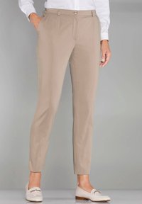 Beige op maat gemaakte broek met een gladde textuur, met een voorgevouwen lijn en zijzakken. Gepaarde met lichtgekleurde loafers.
