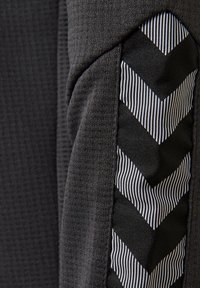 Tejido atlético negro con un acabado texturizado; presenta un acento de rayas en forma de chevrón en negro y blanco a lo largo de un lado.