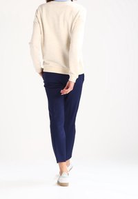 Sweat-shirt beige clair avec texture mouchetée, associé à un pantalon tapered bleu marine. Les chaussures sont blanches avec des accents vert menthe et une semelle texturée.