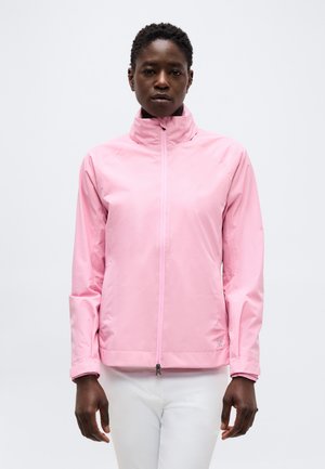 Person wearing a light pink zip-up jacket with high collar and white pants against a plain white background.