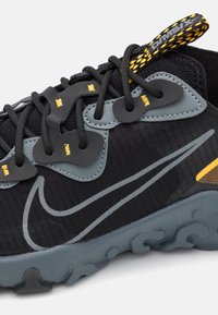 Černá sportovní obuv s texturovaným svrškem, šedými akcenty, žlutými tkaničkami a gumovou podrážkou s vlnkovým vzorem. Boční logo v šedé barvě.