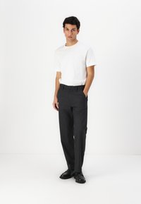 Pantalon gris à coupe ajustée, en tissu lisse, comportant deux poches latérales et des passants de ceinture, associé à un T-shirt blanc uni.