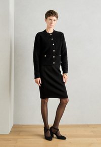 Czarny puszysty kardigan z złotymi guzikami, w zestawie z dopasowaną czarną spódnicą. Uzupełniony czarnymi przezroczystymi rajstopami i sandałami na kostkę.