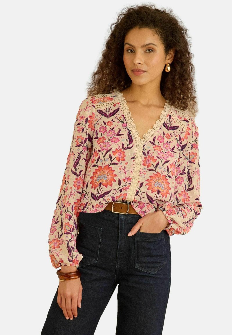 Kvetinová blúzka z jemnej ružovej látky s výstrihom do V, čipkovými detailmi, dlhými rukávmi a farebnými kvetinovými vzormi. Nosená s tmavými džínami.