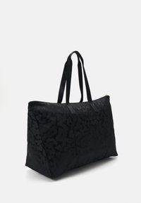 Suuri musta kuvioitu kangaskassi, jossa on pitkät hihnat ja ulkoinen etutasku, esitettynä yksinkertaista valkoista taustaa vasten.