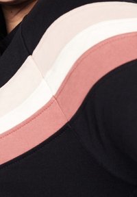 Top negro con rayas diagonales en rosa claro, blanco y rosa empolvado. Textura suave con un diseño ajustado y escote redondo.