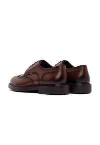 Brązowe skórzane buty typu brogue z detalami wingtip i ciemno-brązowymi, warstwowymi obcasami, przedstawione z niskiego tylnego bocznego kąta.