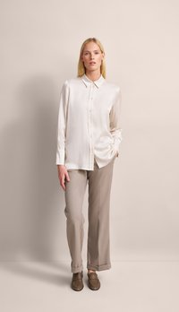 Light beige silk blouse with a button-up front and collar, paired with gray tailored pants and brown loafers. Minimalist design and smooth texture.
