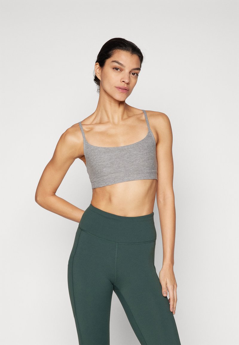 Grå tettsittende crop top med tynne stropper, kombinert med høytlivede mørkegrønne leggings. Glatt stoff med et minimalistisk design.