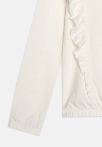 Bílý dlouhý rukáv top vyrobený z měkké bavlny; má volánkový detail podél strany a elastické manžety na konci rukávů.