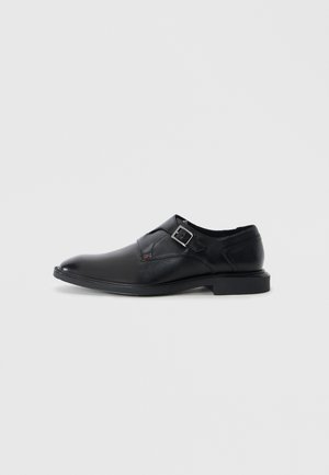 Zapato de dress de cuero negro con punta redondeada, detalle de hebilla lateral, textura suave y tacón bajo. Diseño minimalista y silueta elegante.