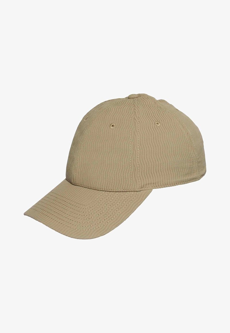 Gorra de béisbol beige con textura, visera curvada y ojales de ventilación, mostrada desde un ángulo lateral sobre un fondo blanco.