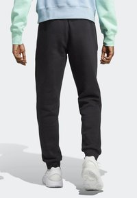 Black sweatpants made of soft, textured fabric, featuring a tapered design and elastic cuffs, paired with white sneakers.