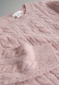 Morbido maglione rosa chiaro a trecce con collo e polsini a coste, disteso in piano che mostra la trama e il motivo dettagliato della maglia.