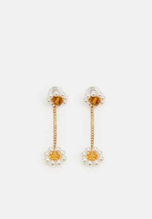 Boucles d'oreilles pendantes en chaîne d'or avec des gemmes couleur ambre entourées de petites perles blanches aux deux extrémités sur fond blanc.