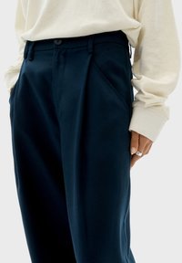 Pantaloni blu navy realizzati in un tessuto liscio, con una vestibilità rilassata, pieghe frontali, tasche laterali e chiusura con bottone in vita.
